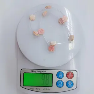 Pink carved shell rose flower beads DIY jewelry accessory detail shot showing weight on scale.