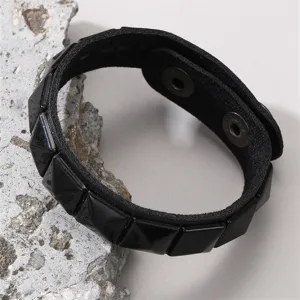 Nahaufnahme eines schwarzen Punk Nieten Lederarmbands mit Druckknopf auf strukturierter Oberfläche