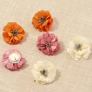 Nahaufnahme mehrfarbiger Stoffblumen-Accessoires mit zarten Lagenblättern und Perlen.
