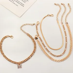 Set of four gold-toned layered anklets featuring dainty chains and a sparkling letter charm.