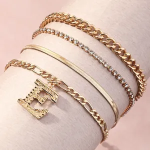 Close-up detail of multi-layer gold chain bracelets set with rhinestone and letter charm.