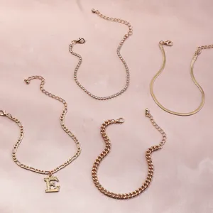 Set of 4 gold fashion anklets with crystal letter E pendant, tennis chain, and chic chains.