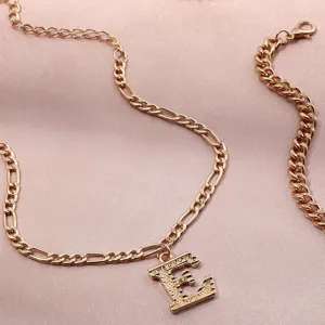 Detailed view of gold-tone figaro chain anklet adorned with a sparkling rhinestone letter E pendant.