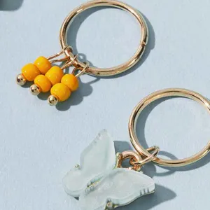Detailaufnahme von goldenen Haarringen mit gelben Perlen und Schmetterlingsanhängern.