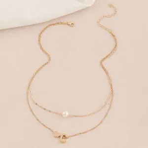Nahaufnahme einer zweilagigen Goldkette mit Perle und einem Buchstaben C Anhänger.