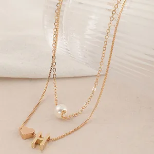 Detailaufnahme einer goldenen doppelten Halskette mit Perle, Herz und H-Anhänger.
