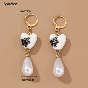 Elegant gold leverback drop earrings featuring white heart charm and dangling pearl.