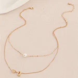 Nahaufnahme Detail der doppelreihigen Goldkette mit Perle und Buchstabe Q Herz Anhänger.