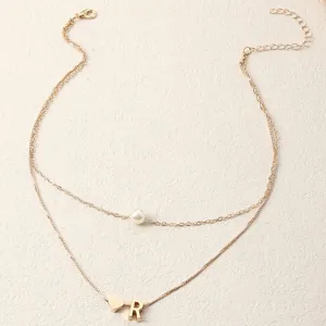 Detailaufnahme einer doppellagigen Goldkette mit Perlenanhänger und Buchstaben-R-Anhänger.