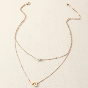 Goldfarbene mehrlagige Kette mit Perlenanhänger und Buchstabenherz-Charm, Schmuck-Detailaufnahme.
