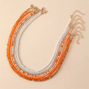 Close-up detail of multi-strand bohemian seed bead necklaces in orange and white tones.