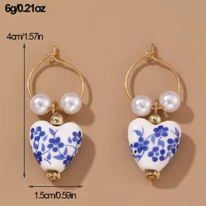 Detailed shot of blue and white porcelain heart earrings with pearls and gold hoop.