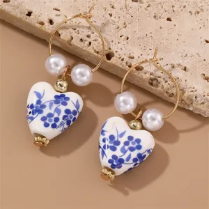 Close-up detail of blue and white porcelain heart earrings featuring elegant pearls and gold hoops.