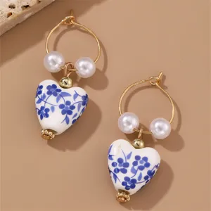 Detailed view of elegant blue and white porcelain heart earrings with pearls and gold hoops.