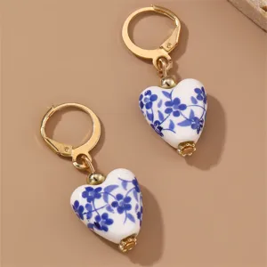 Close-up detail shot of vintage blue and white porcelain floral heart earrings with gold hoop design.