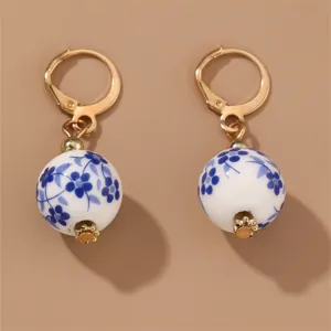 Close-up of elegant blue and white porcelain floral bead earrings with gold leverback hooks.