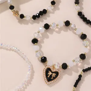Schwarz-weißes Perlenarmband-Set mit bezauberndem Schleifen-Herz-Anhänger und Kristall-Akzenten.