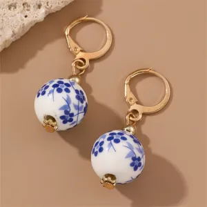 Close-up of elegant blue and white porcelain ball earrings with gold-toned leverback hooks.