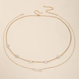 Gegliederte Gold-Taillenkette mit weißen Gänseblümchen und Perlenanhänger am Strand.