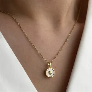 Nahaufnahme einer goldenen Halskette mit Perlmuttanhänger und goldenem Herz im Detail.
