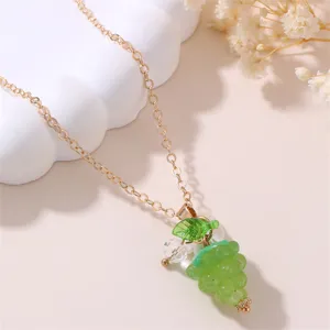 Close-up detail of the green resin grape pendant necklace with a delicate gold chain and leaf charm.