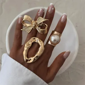 Goldene Statement Ring Set mit edler Schleife, unregelmäßigem geschmolzenem Metall und Perle.