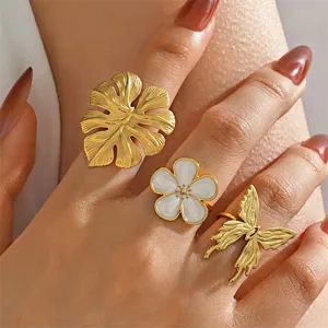 Elegantes vergoldetes Metallring-Set mit Monstera-Blatt, weißer Blume und Schmetterling-Motiv.
