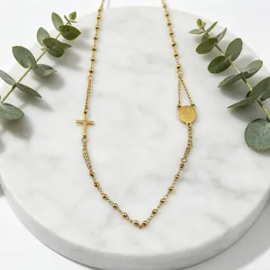 Vue de détail rapprochée du collier chapelet en acier inoxydable doré posé sur marbre blanc.