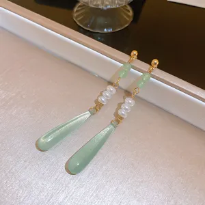 Primo piano di eleganti orecchini a goccia verdi con perle e catena dorata in dettaglio.