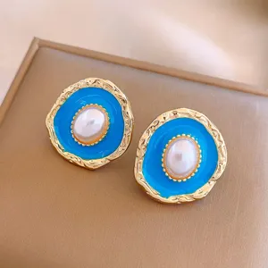 Vintage oval pearl earrings featuring vibrant blue enamel and textured gold-tone outer edges.