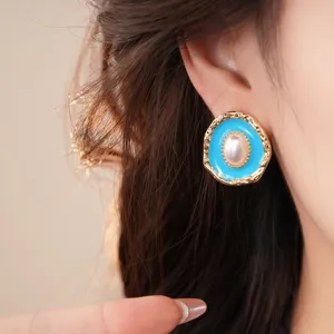 Detailed close-up of vintage gold-rimmed blue enamel pearl earrings worn by model.