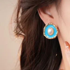 Closeup of retro oval pearl earrings with vibrant blue oil drop and intricate gold edge details.