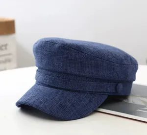 Close-up of a stylish dark blue linen baker boy cap on white table, textured fabric design.