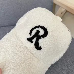 Detailed view of white sherpa baseball cap with black letter R embroidery for winter.
