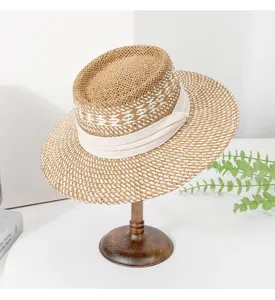 Detailed view of the woven straw hat with beige ribbon and unique dented top design.