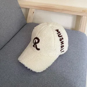 Detailed view of cream lamb wool baseball cap with brown R letter embroidery and side text.