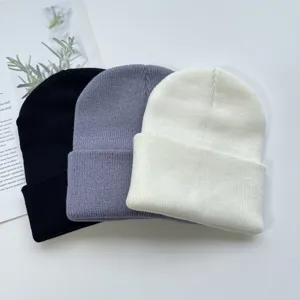 Close-up detail of three solid color knit beanies in black, grey, and white, cozy autumn winter.