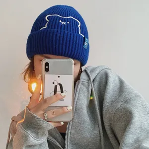 Close-up detail shot of the royal blue knit beanie featuring cute bear embroidery and a side tag.