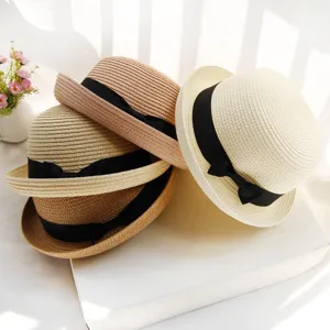 Detail view of stylish straw dome sun hats with black ribbon bow, stacked together neatly.
