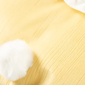 Detail view of cute yellow pet clothing featuring a fluffy white rabbit tail pom-pom design.