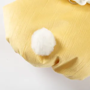 Cute rabbit tail pet winter coat detail, yellow textured fabric with fluffy white pom-pom.