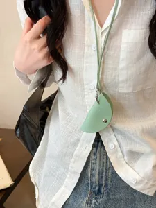 Detail view of a mini leather dumpling pouch key case in light green with a chic lanyard strap.