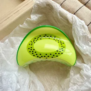 Close-up of a vibrant kiwi print hair claw clip resting on soft white tissue paper