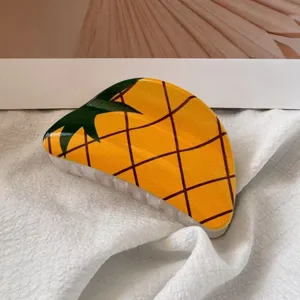 Close-up of vibrant yellow pineapple print hair claw clip on soft white fabric background
