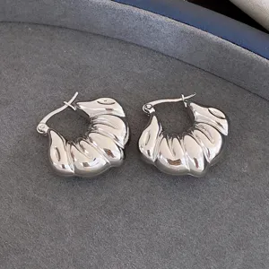 Gros plan détaillé de boucles d'oreilles créoles tendance en argent avec texture nervurée.