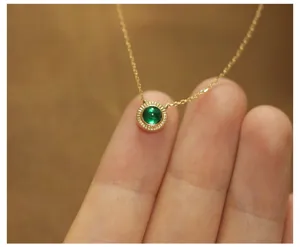 Macro detail view of a round green emerald pendant on a 14K gold plated silver chain