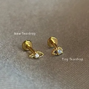 Nahaufnahme von goldenen Teardrop-Labret-Steckern mit Zirkonia auf grauem Stoff