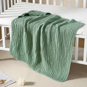 Soft green cotton muslin baby swaddle blanket draped on a white crib in a nursery.