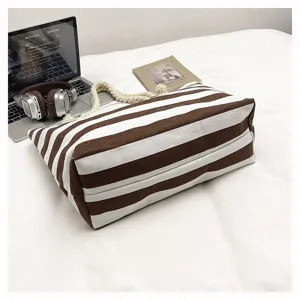 Detailansicht der braun-weiß gestreiften Canvas-Einkaufstasche mit Hanfseilgriffen auf Bett.