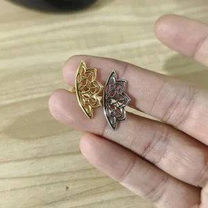Nahaufnahme von minimalistischen Lotusblumen-Ohrsteckern in Gold und Silber auf der Hand.